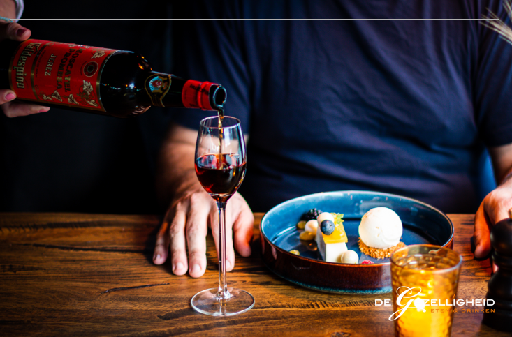 A glass of red wine being poured alongside a plated dessert